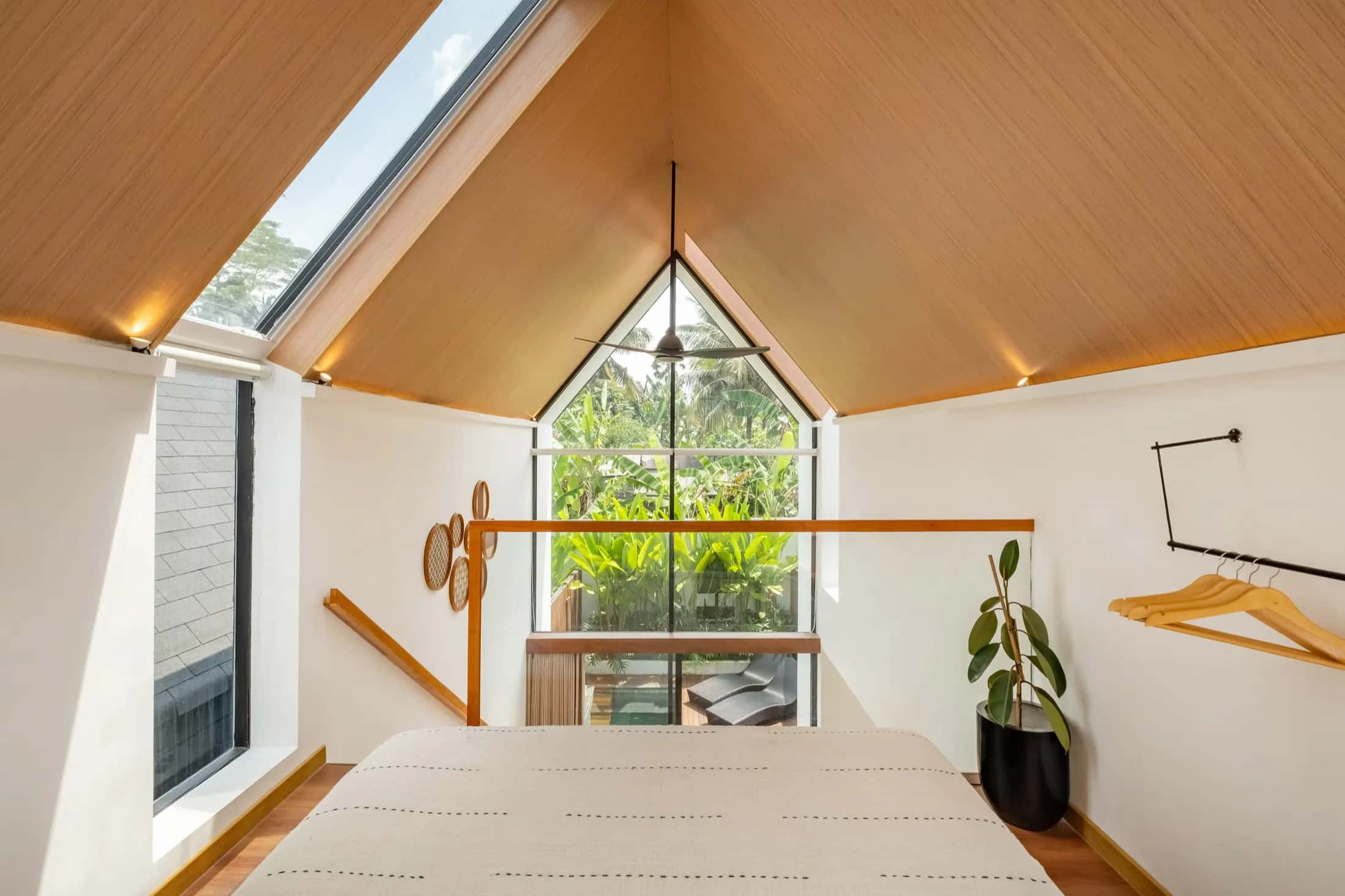 Mezzanine villa bedroom looking toward the triangular apex window under a warm timber ceiling