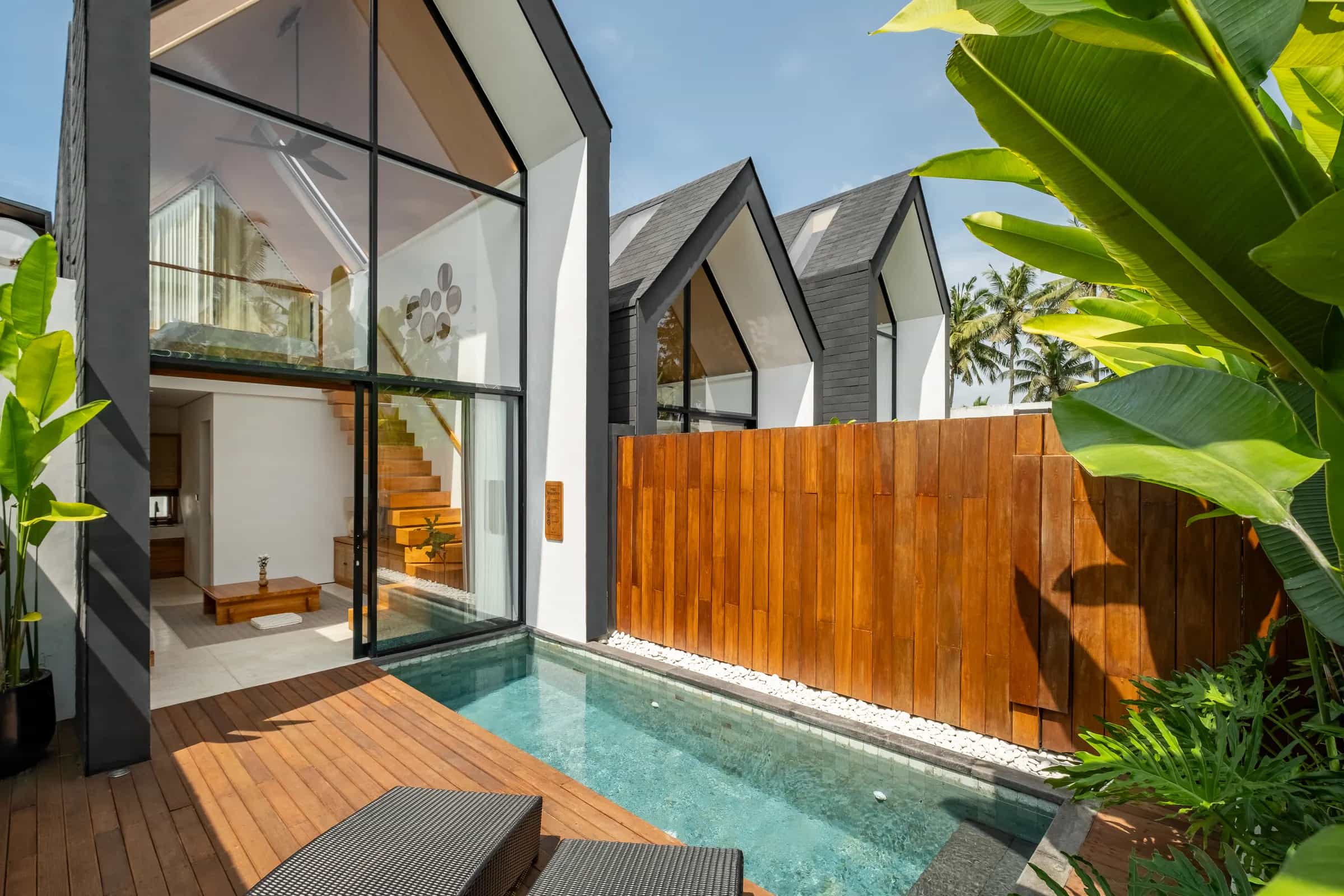 Mezzanine villa’s glass A-frame and pool deck, with the neighbouring A-frame roofs and banana leaves