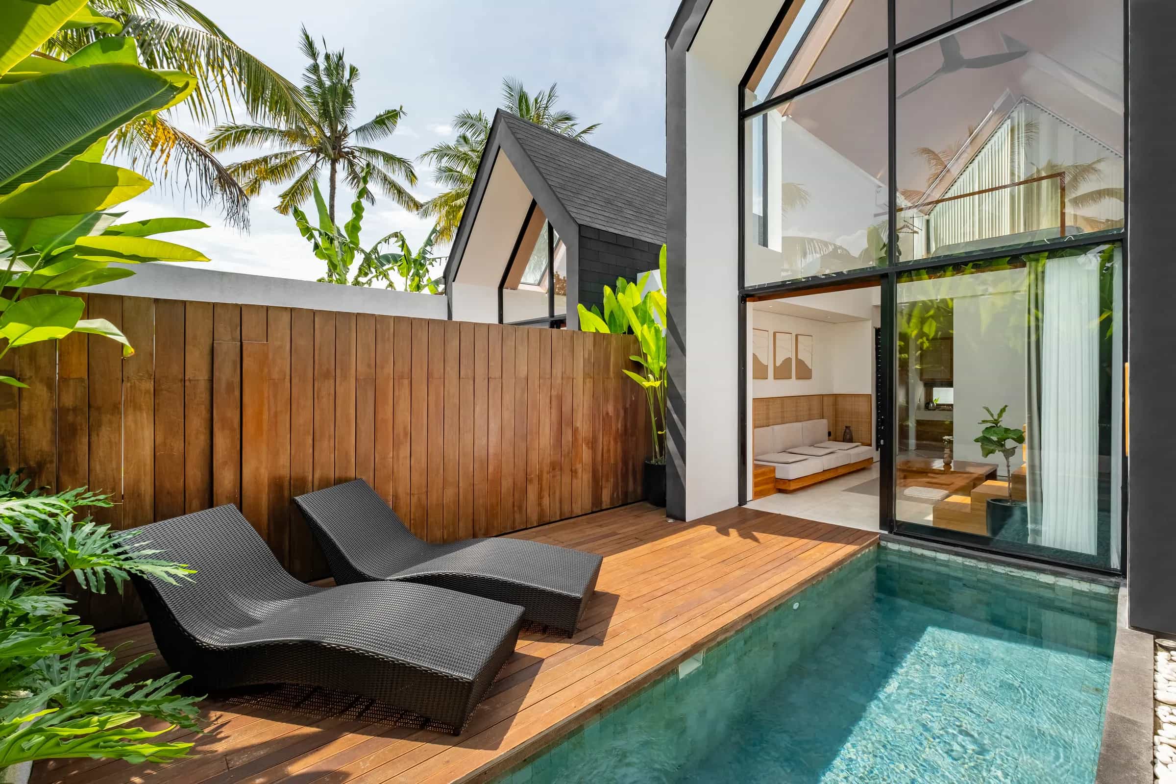 Mezzanine villa's private pool and teak deck with two loungers, coconut palms and an A-frame roofline beyond
