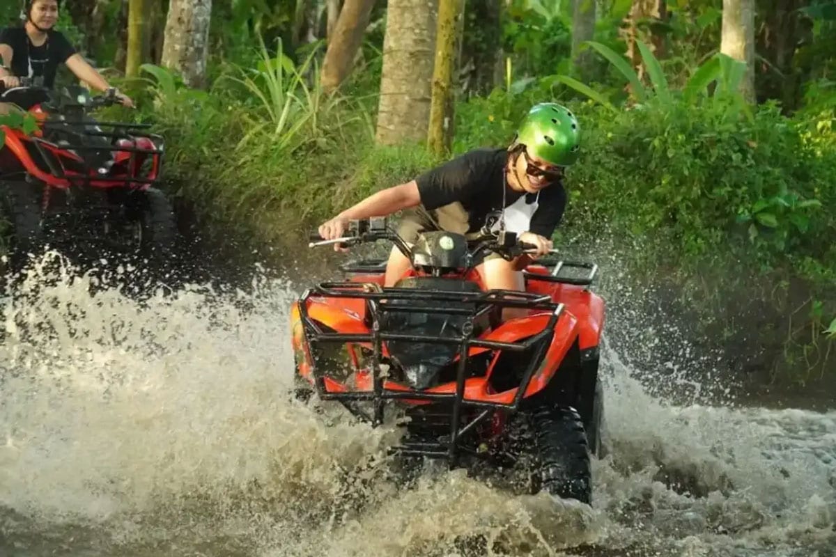 Rider on an orange ATV quad bike splashing through a jungle river in Ubud