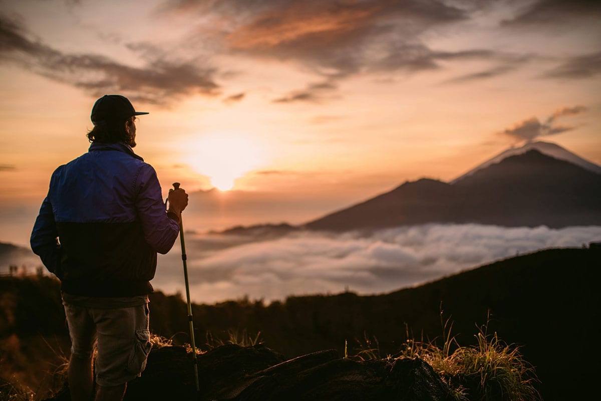 Solo trekker with hiking pole watching the sunrise over Mount Agung from the summit of Mount Batur