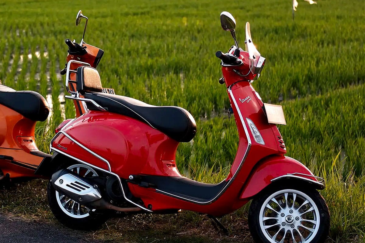 Red Vespa scooter parked in front of lush green rice fields at golden hour